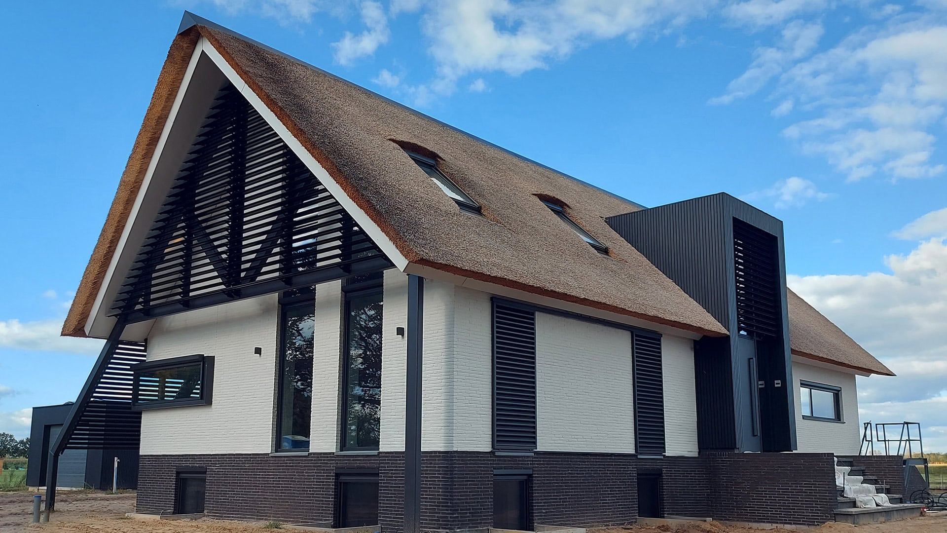 Moderne woonboerderij met kantelbare lamellen in de puntgevel, een risaliet en schuifpanelen aan de voorzijde